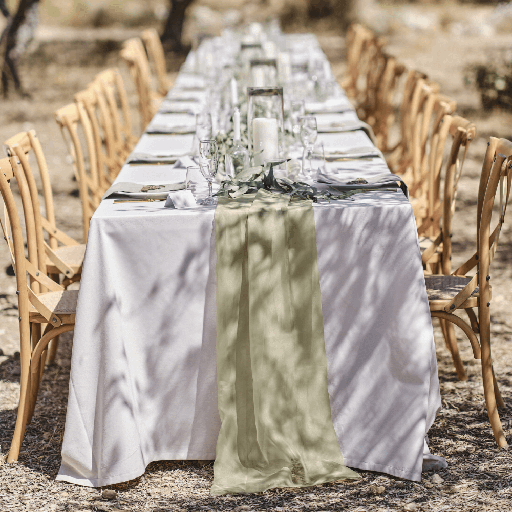 Tafel met wit tafelkleed en sage tafelloper staat in een veld met houten stoelen