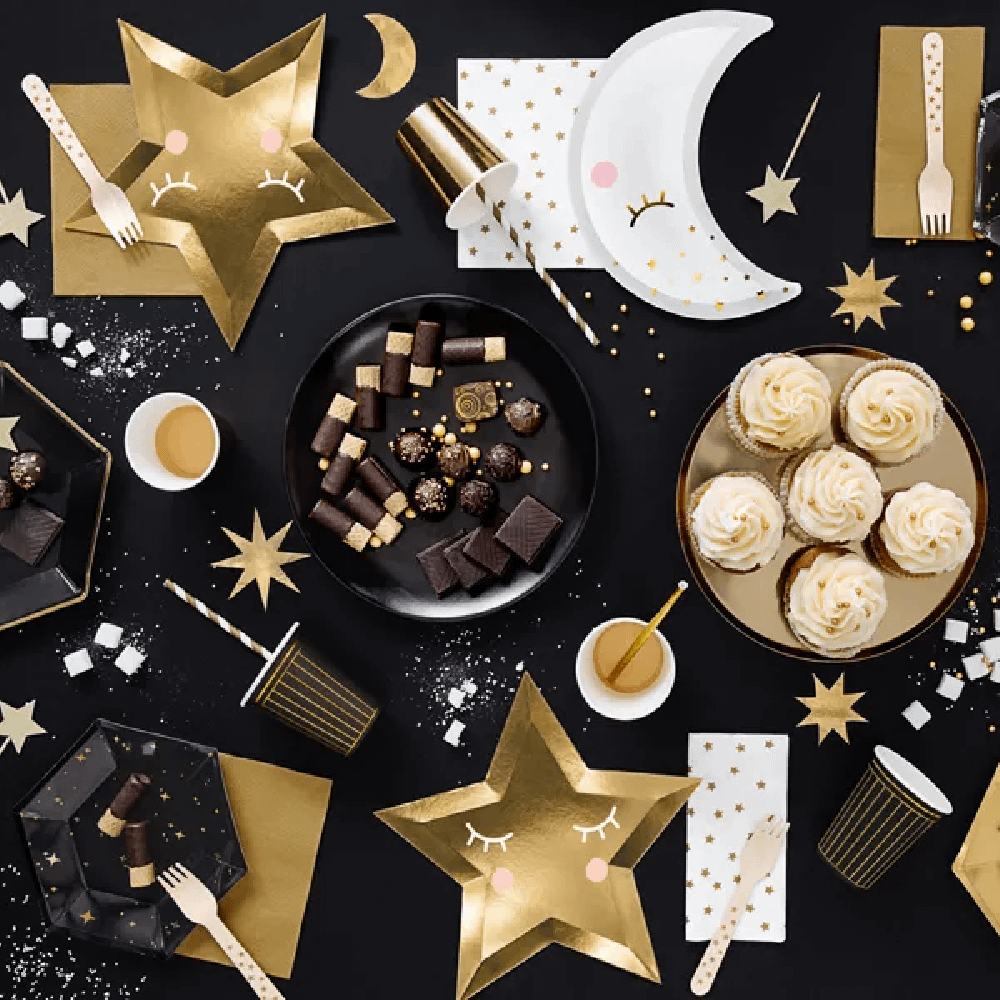 Zwarte en gouden versiering op een zwarte tafel bedekt met cupcakes, servetten, bordjes en bekers