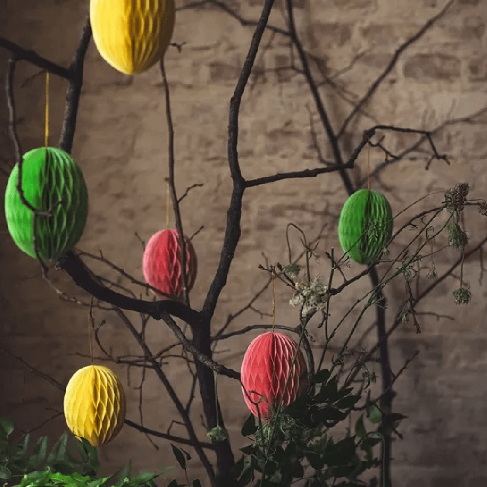Honeycomb paaseieren in het geel, groen en rood hangen aan donkerbruine takken voor een bakstenen muur