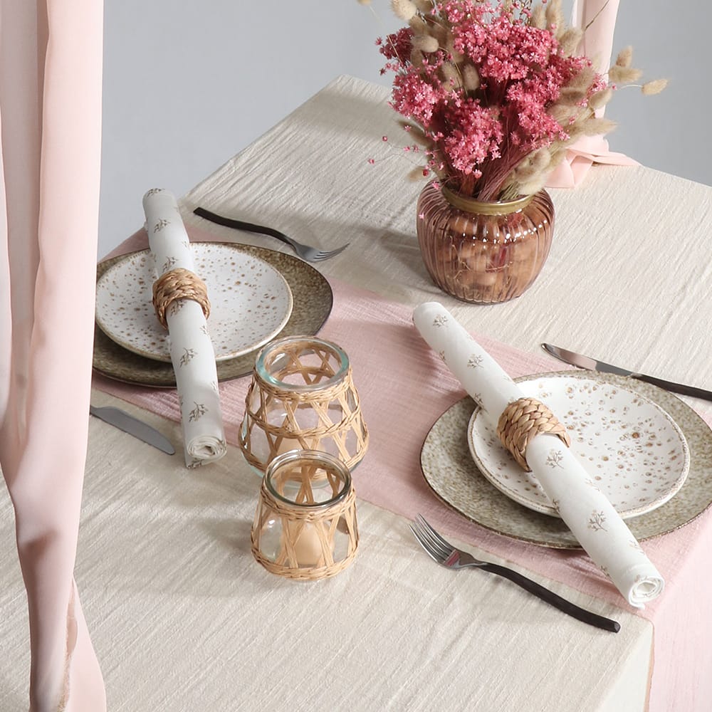 Tafel versierd met bloemen, borden met servetten en rieten servettenringen