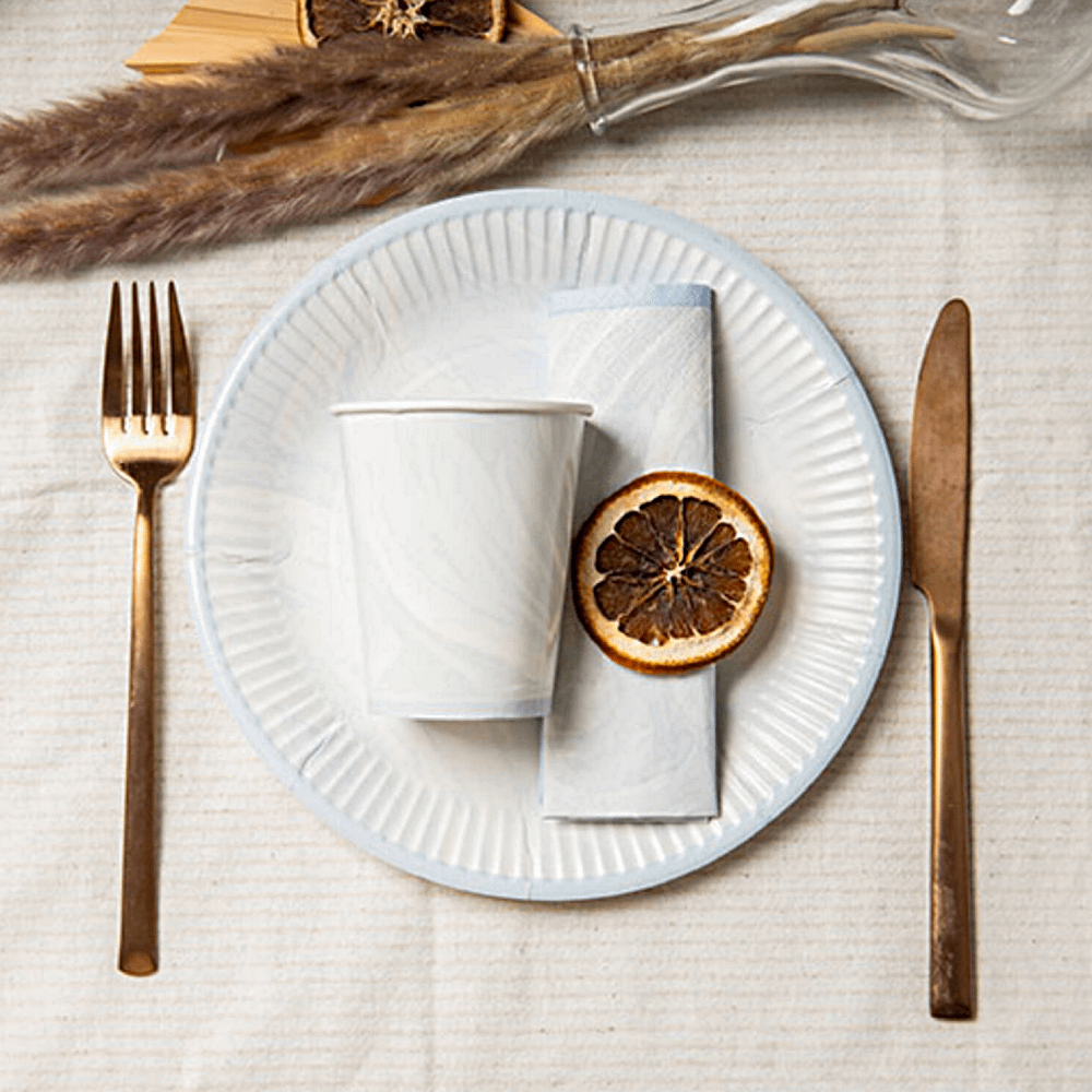 Marmeren blauwe bordjes en beker ligt naast goud bestek op een ivoren tafelkleed met een verbrande sinaasappel
