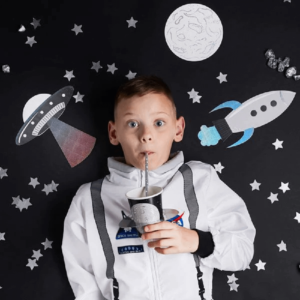 Jongetje in een astronautenpak ligt po een zwarte ondergrond tussen raketten, sterren en een planeet