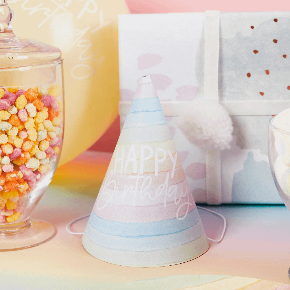Regenboog feesthoedje i npasteltinten staat voor een glazen pot met snoep en een cadeautje met wit lint
