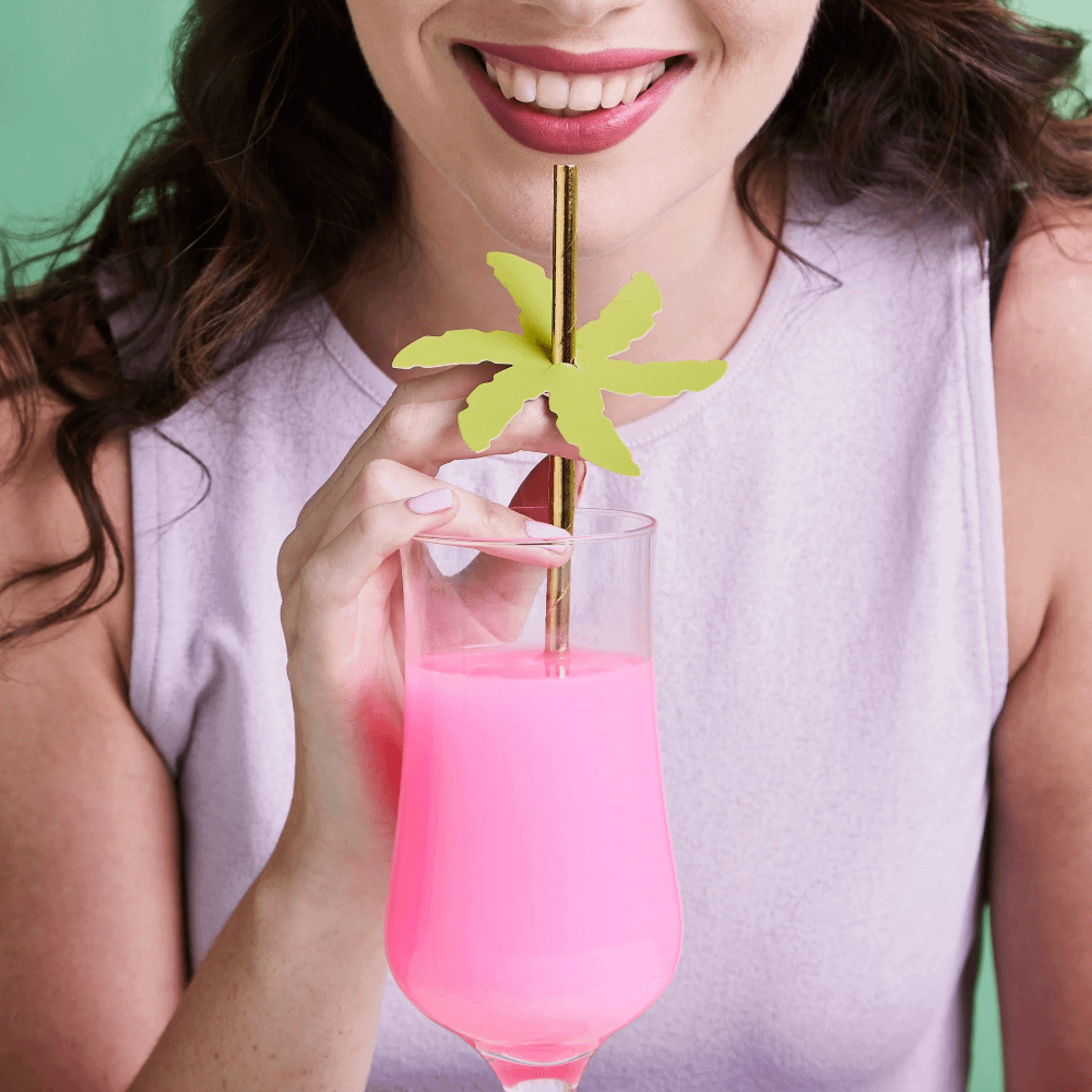 Vrouw neemt een slok uit een glas met roze drinken met een gouden rietje met palmblad
