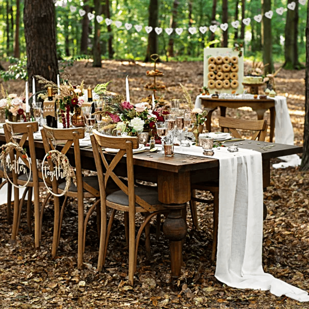 Houten tafel staat in een bos in de herft en is versierd met bloemen, een witte tafelloper en een donut wall