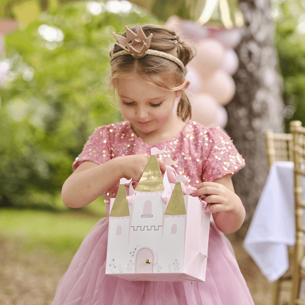 Meisje in roze glitterjurk houd een cadeautasje vast in de vorm van een kasteel en staat in een bos