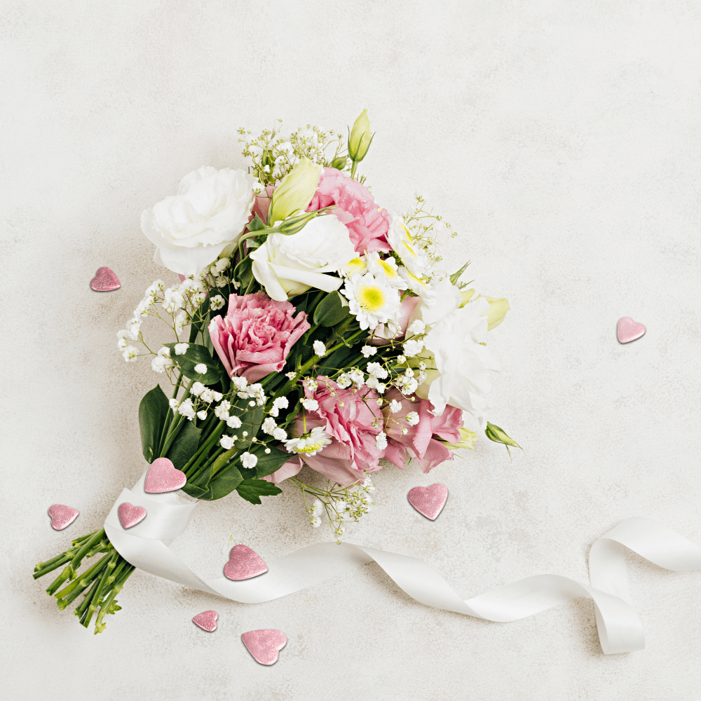 Bosje bloemen met witte en roze rozen en madeliefjes ligt op een wit kleed met confetti hartjes