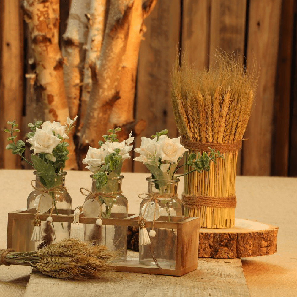 Glazen vaasjes in een houten houder gevuld met eucalyptus takjes en witte rozen