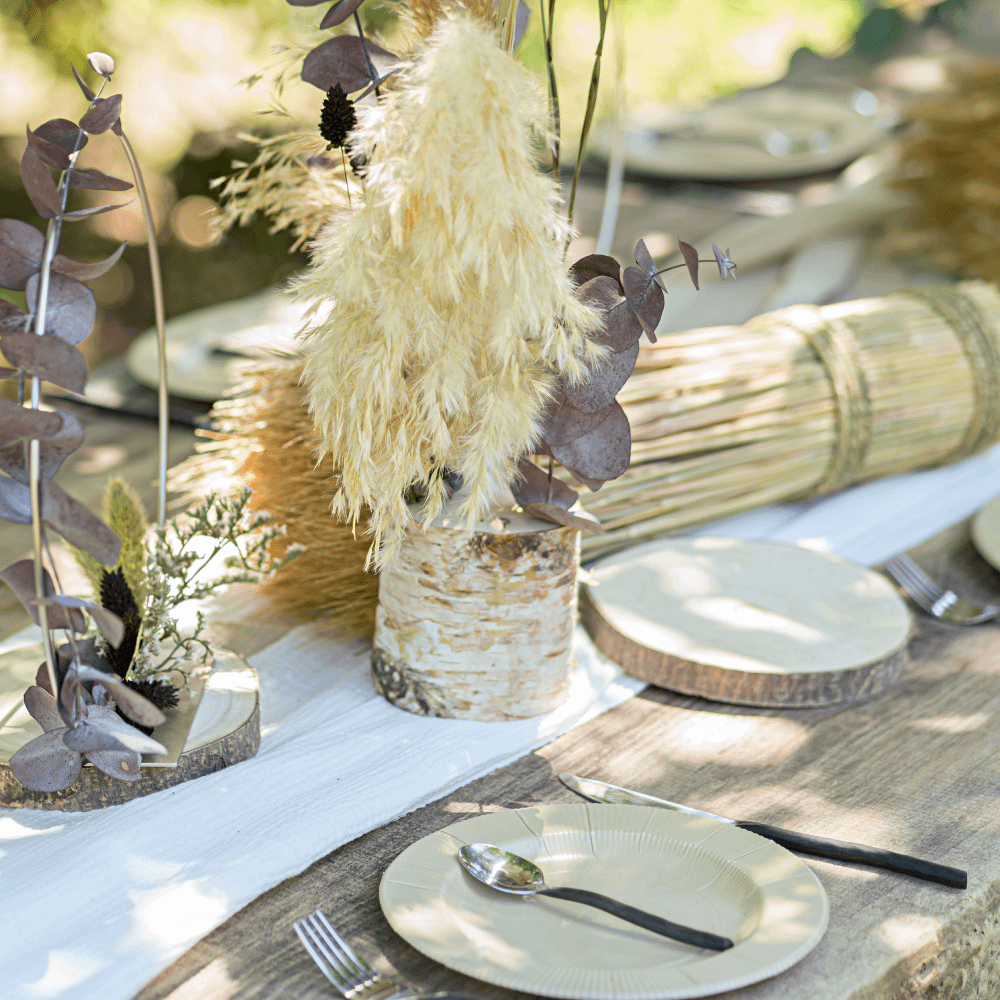 Houten tafel staat buiten en is versierd met droogbloemen, veren en boomstammen