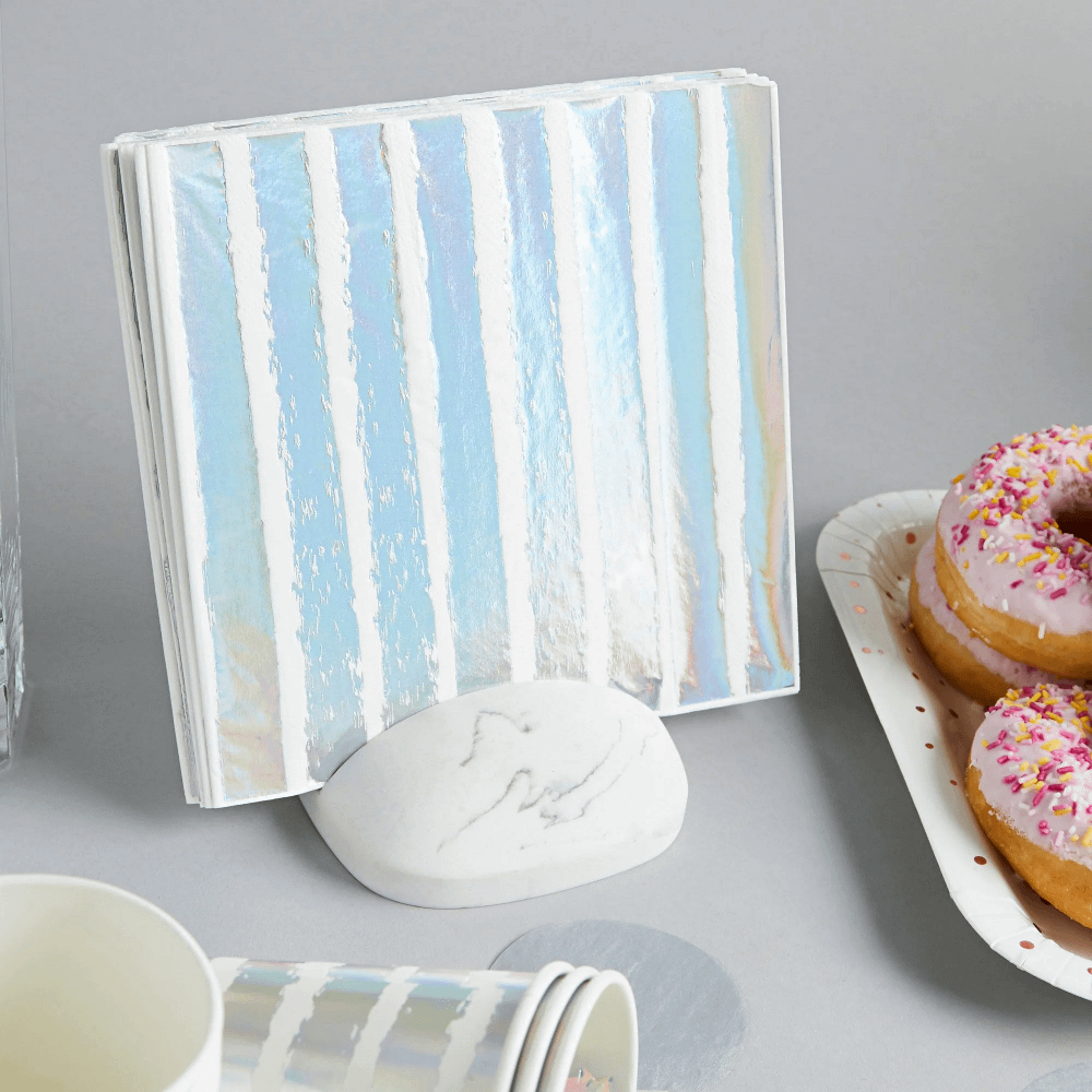 witte en iridescent gestreepte servet zit in een witte servet houder naast een schaal roze donuts