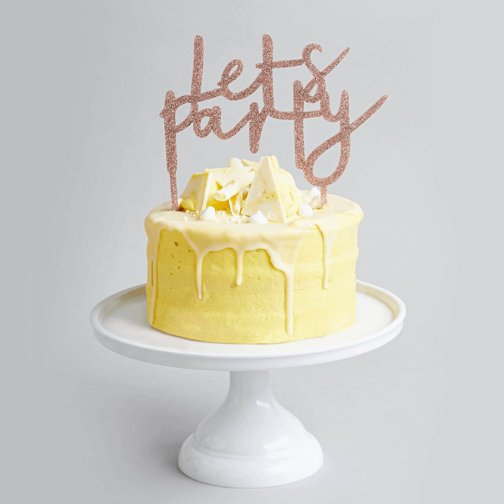 glitter taart topper in het rose goud zit in een gele taart en staat op een wit plateau