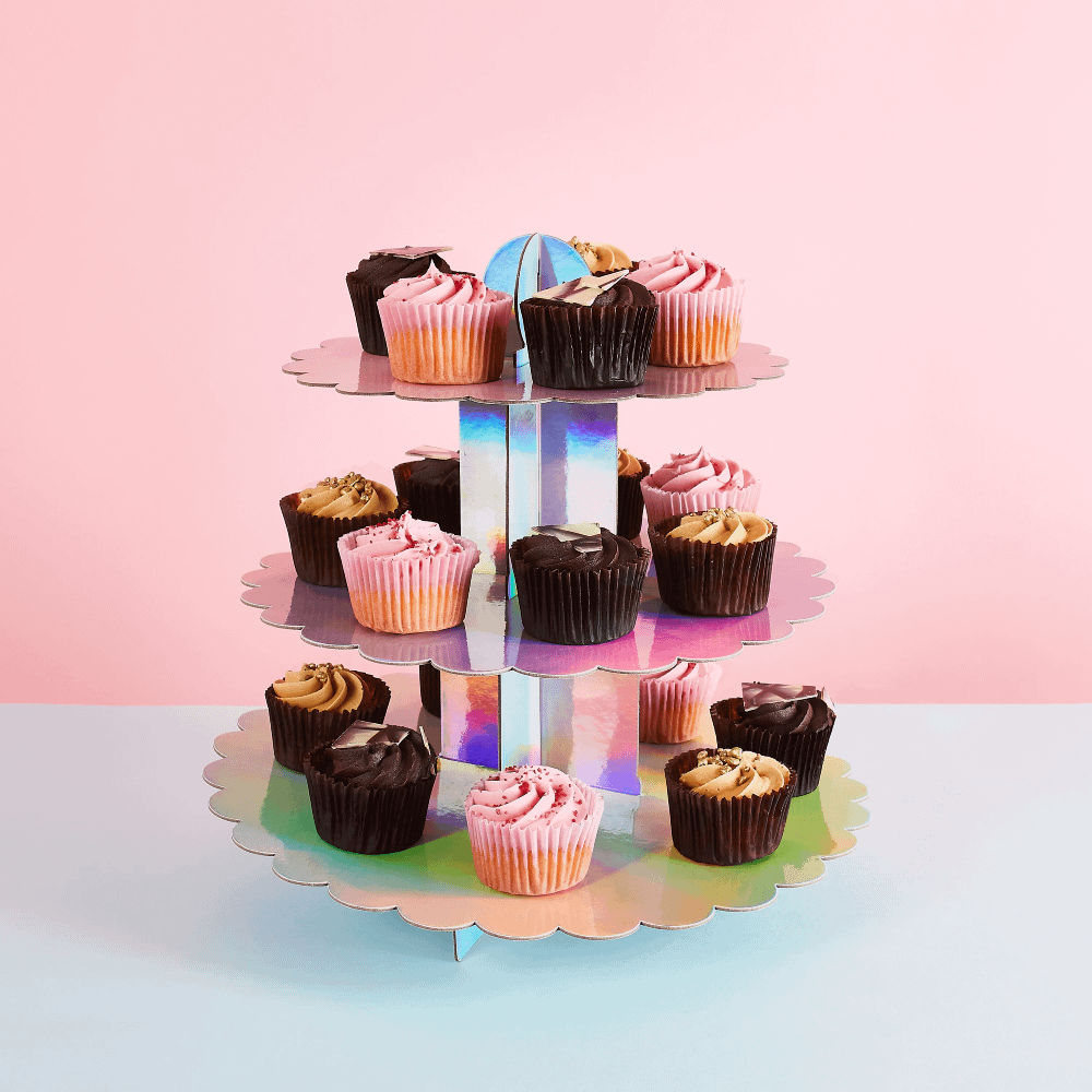 iridescent cake standaard gevuld met bruine en roze cupcakes staat op een blauwe tafel