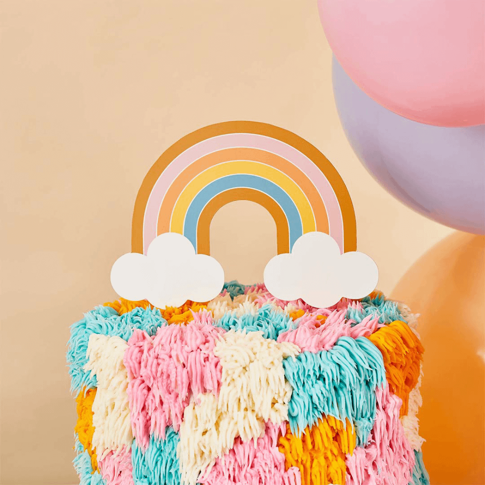 Regenboog taart topper zit in een regenboog taart en staat voor gele smileyballonnen en een perzikkleurige muur