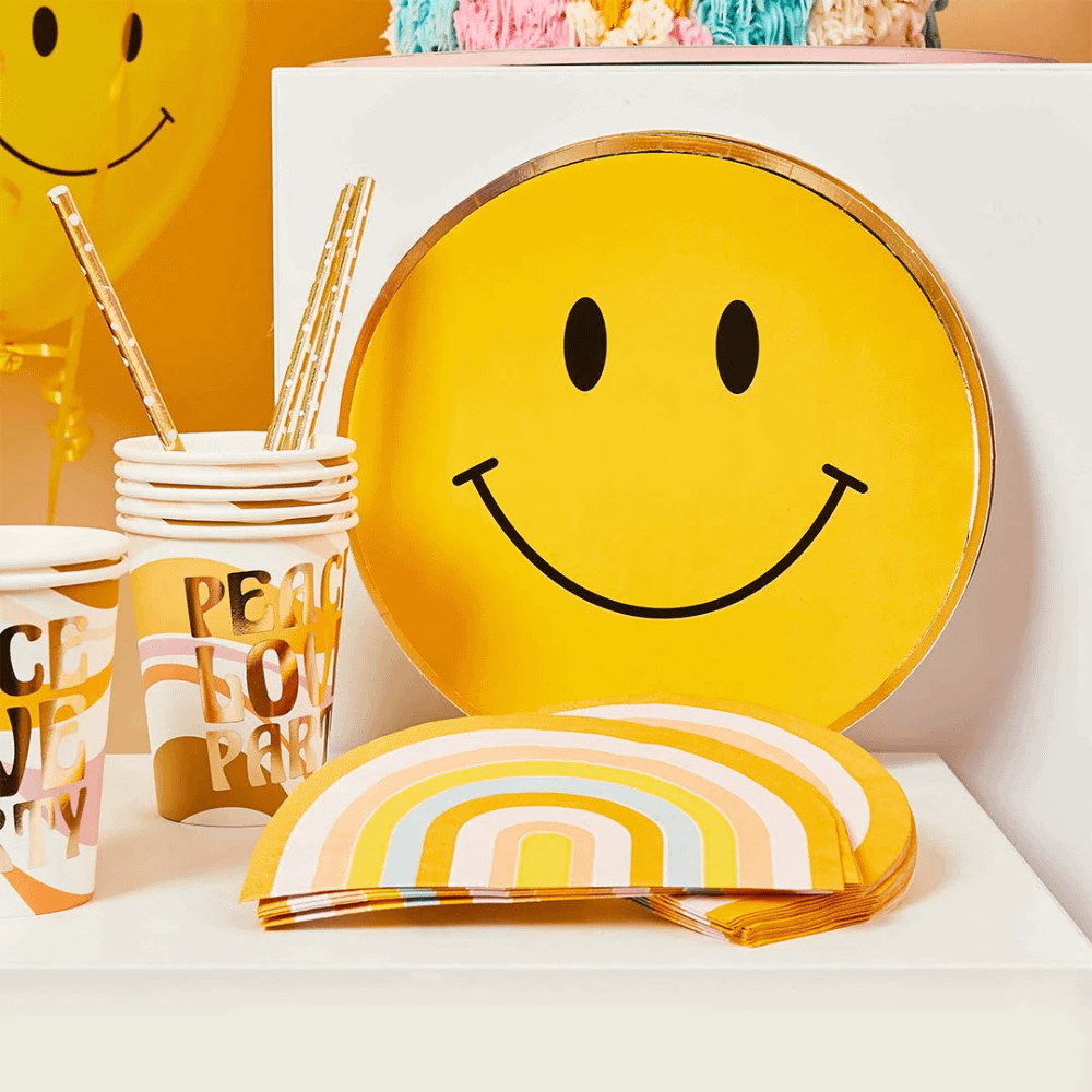 Geel smiley bordje met gouden rand staan achter regenboog servetten en bekers