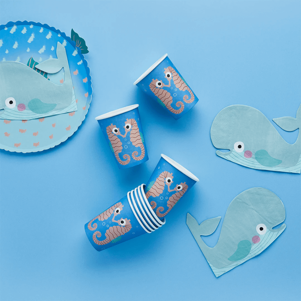 papieren bekers met zeepaardjes erop liggen op een blauwe achtergrond naast een kogelvis bordje en walvis servetten