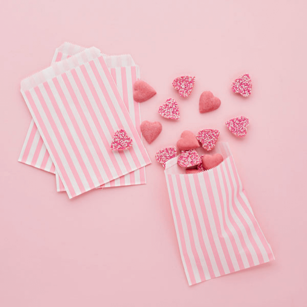 roze achtergrond met roze en wit gestreepte zakjes gevuld met snoep hartjes