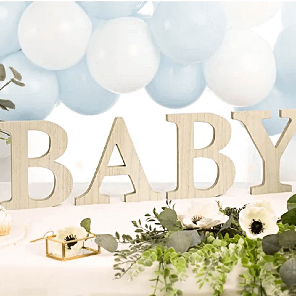 houten letters baby onder een wit met blauwe ballonnenboog naast groene bladeren