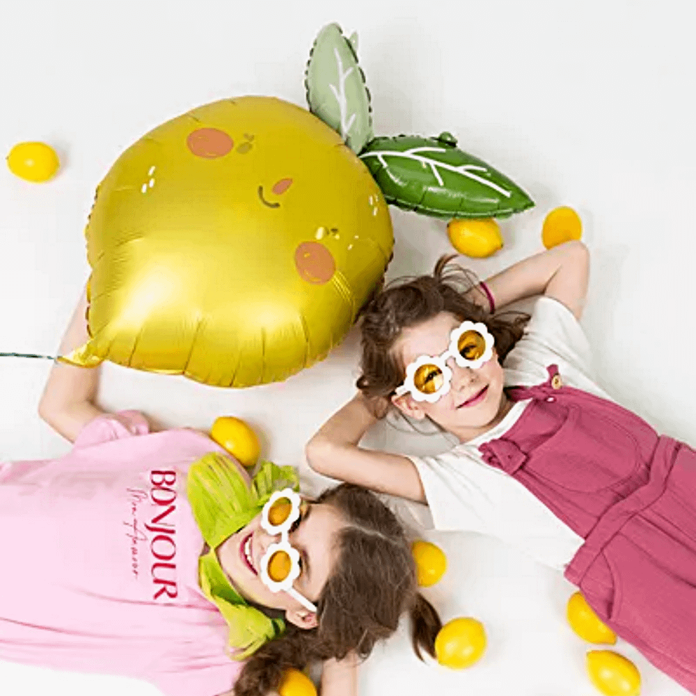 twee meisjes liggen op een witte achtergrond naast citroenen en een folieballon in de vorm van een lachend citroentje