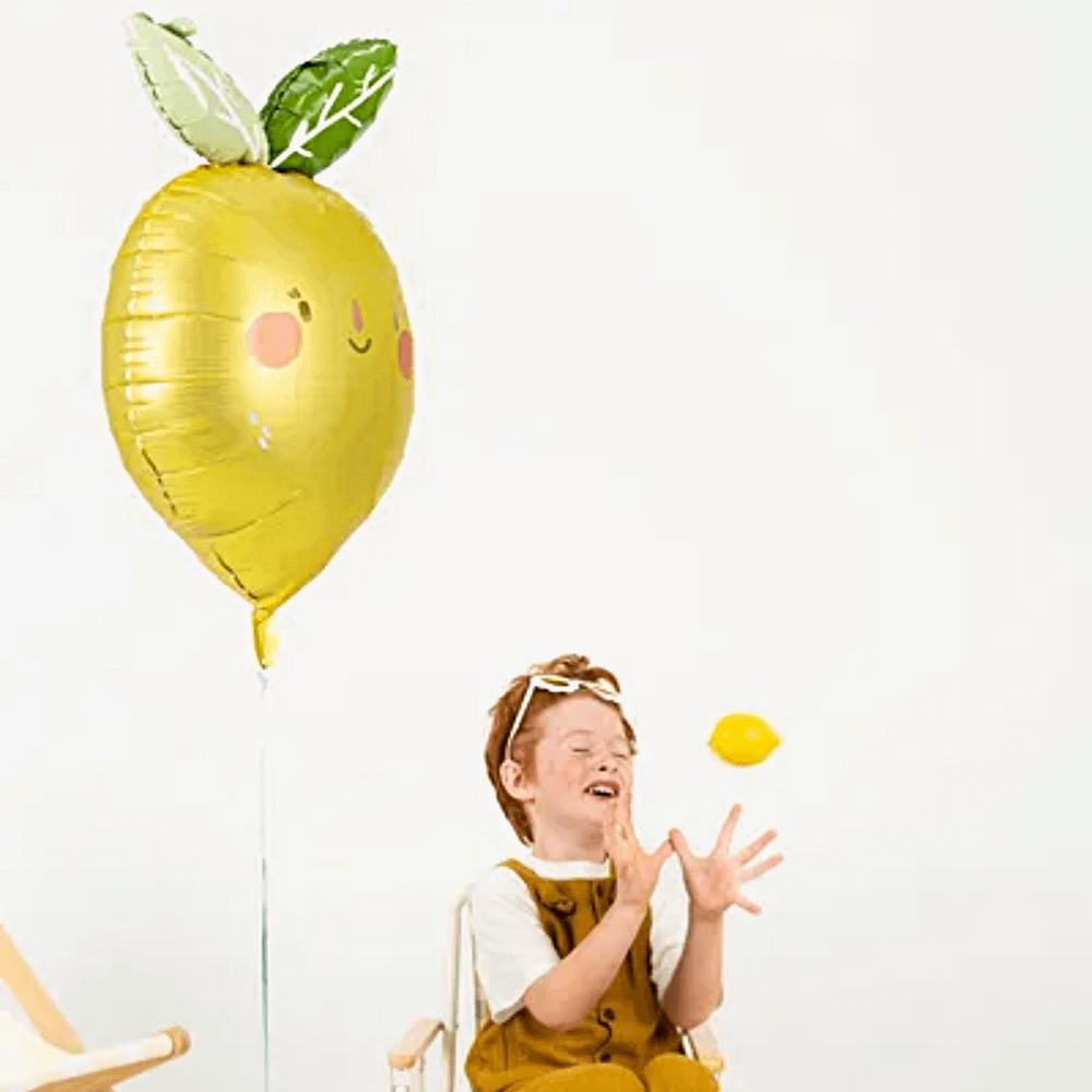 jongen met oranje haar en zonder ziel speelt met een citroen en zit op een tuinstoel naast een gele citroen ballon