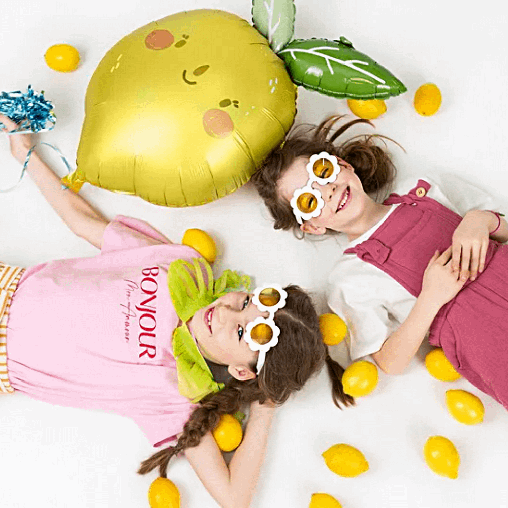 twee meisjes liggen op een witte achtergrond naast citroenen en een folieballon in de vorm van een lachend citroentje