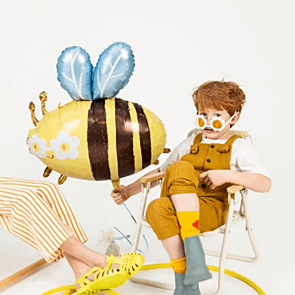 Cool kind met madeliefjes zonnebril houd een hommel ballon vast en zit op een gele tuinstoel