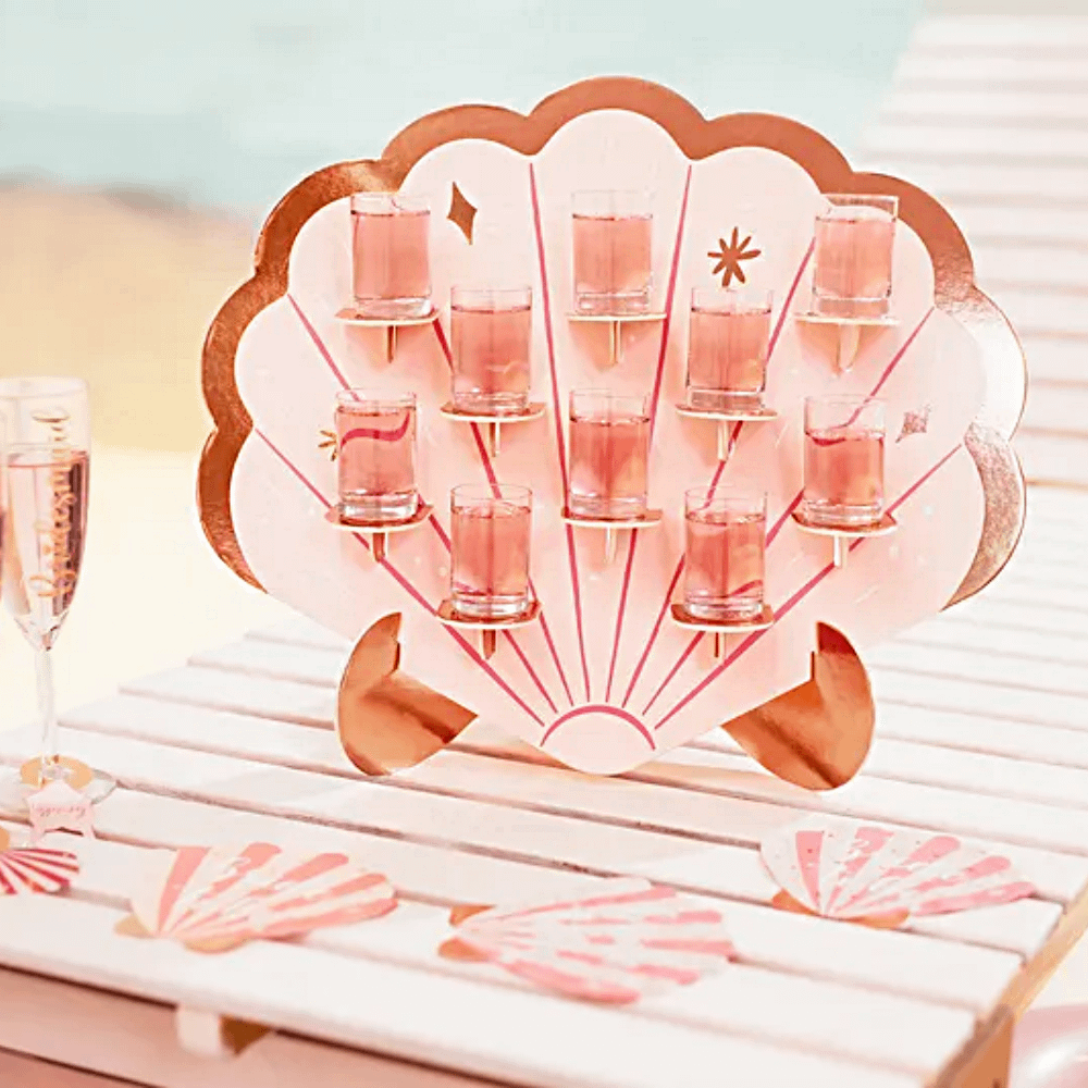 roze schelp met roze shotjes en iridescent rand staat op een houten tafel op het strand