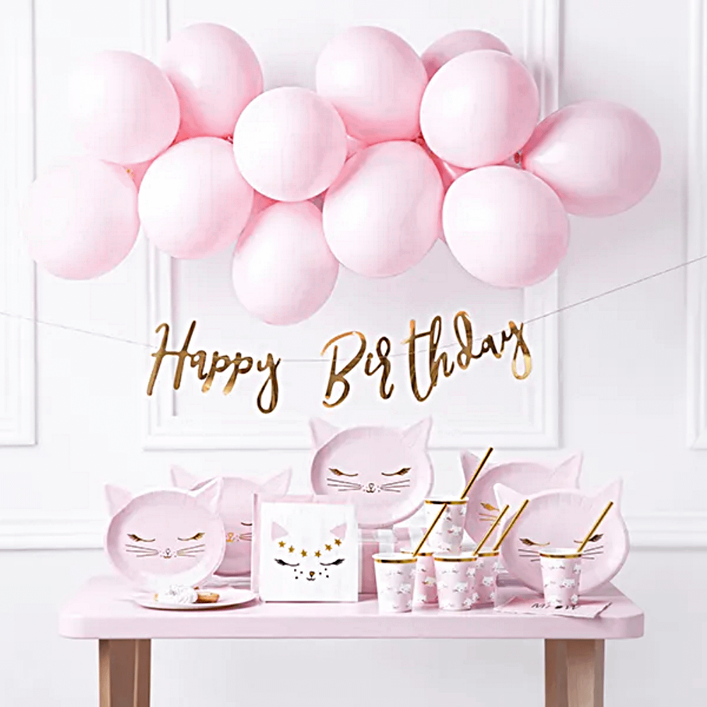 lichtroze ballonnenboog hangt boven een tafel met roze en gouden kattenversiering
