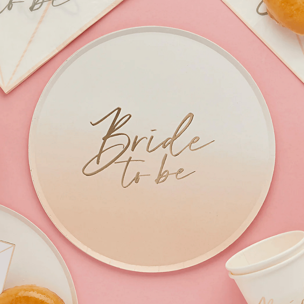 wit en perzik ombre bordjes met gouden tekst bride to be op een roze tafel