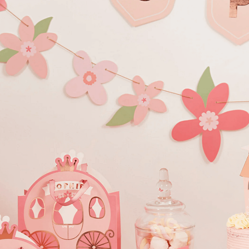 Roze bloemenslinger hangt aan een beige muur achtern een cadeautasje in de vorm van een koets en een glazen pot met spekjes