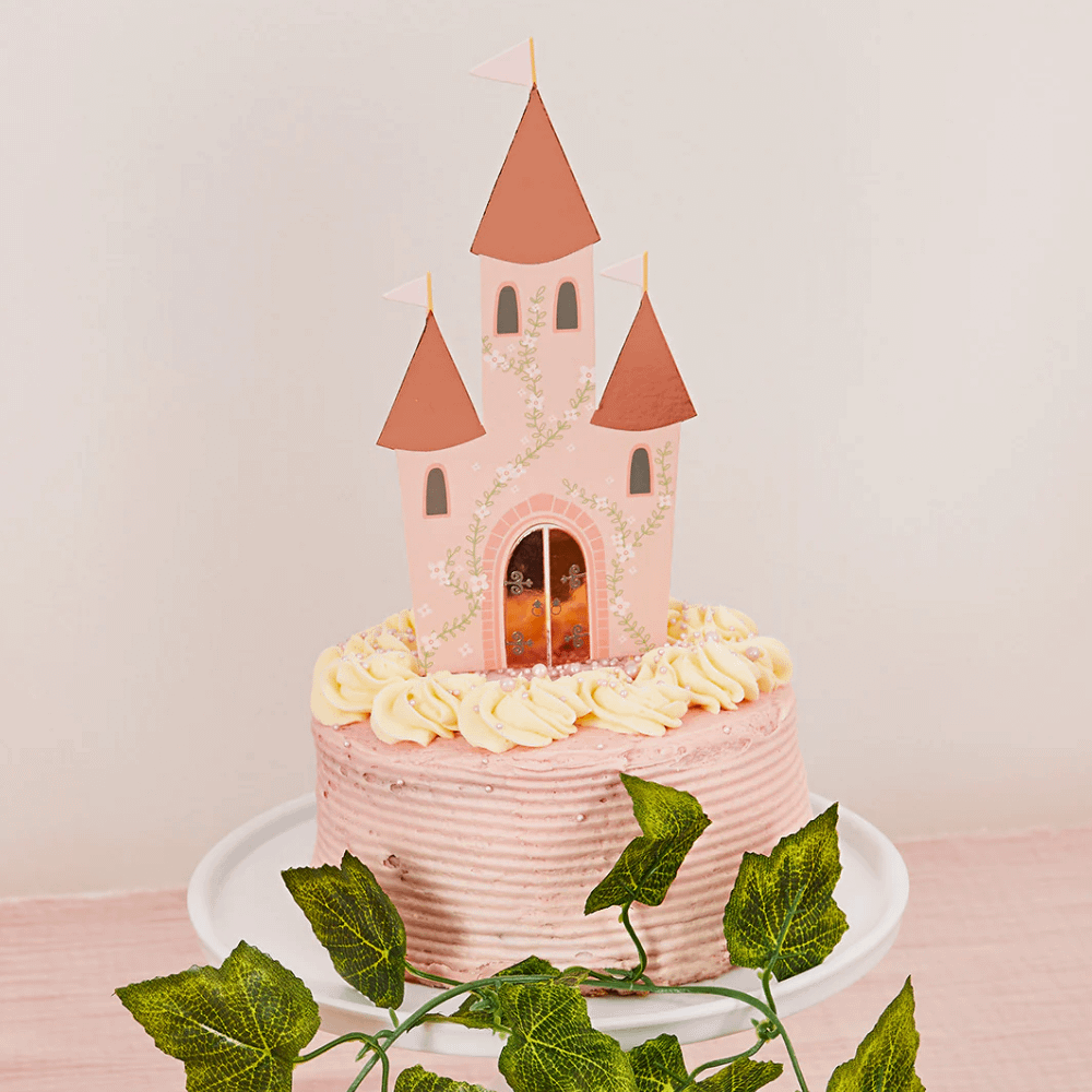 Roze taart op een wit plateau versierd met een kasteel in het rose en rosé goud met bloemen en eucalyptus