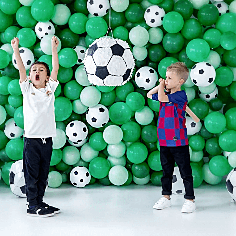 Muur van groene ballonnen en voetbal ballonnen met twee jongens die op een voetbal pinata slaan