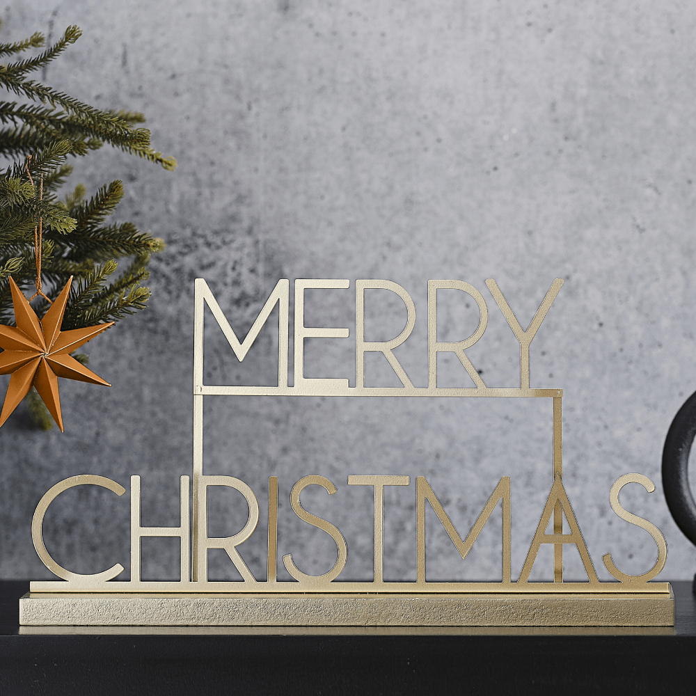 Gouden bordje van metaal met de tekst merry christmas staat op een zwarte tafel voor een grijze muur