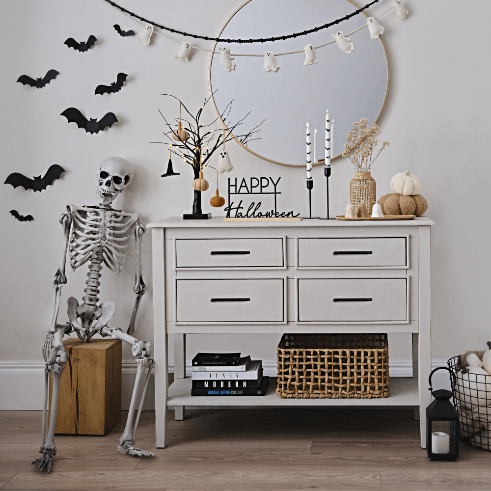 Wit kastje versierd met halloween versiering zoals kaarsen, een skelet, stoffen pompoenen en spookjes en een zwart bordje met de tekst happy halloween