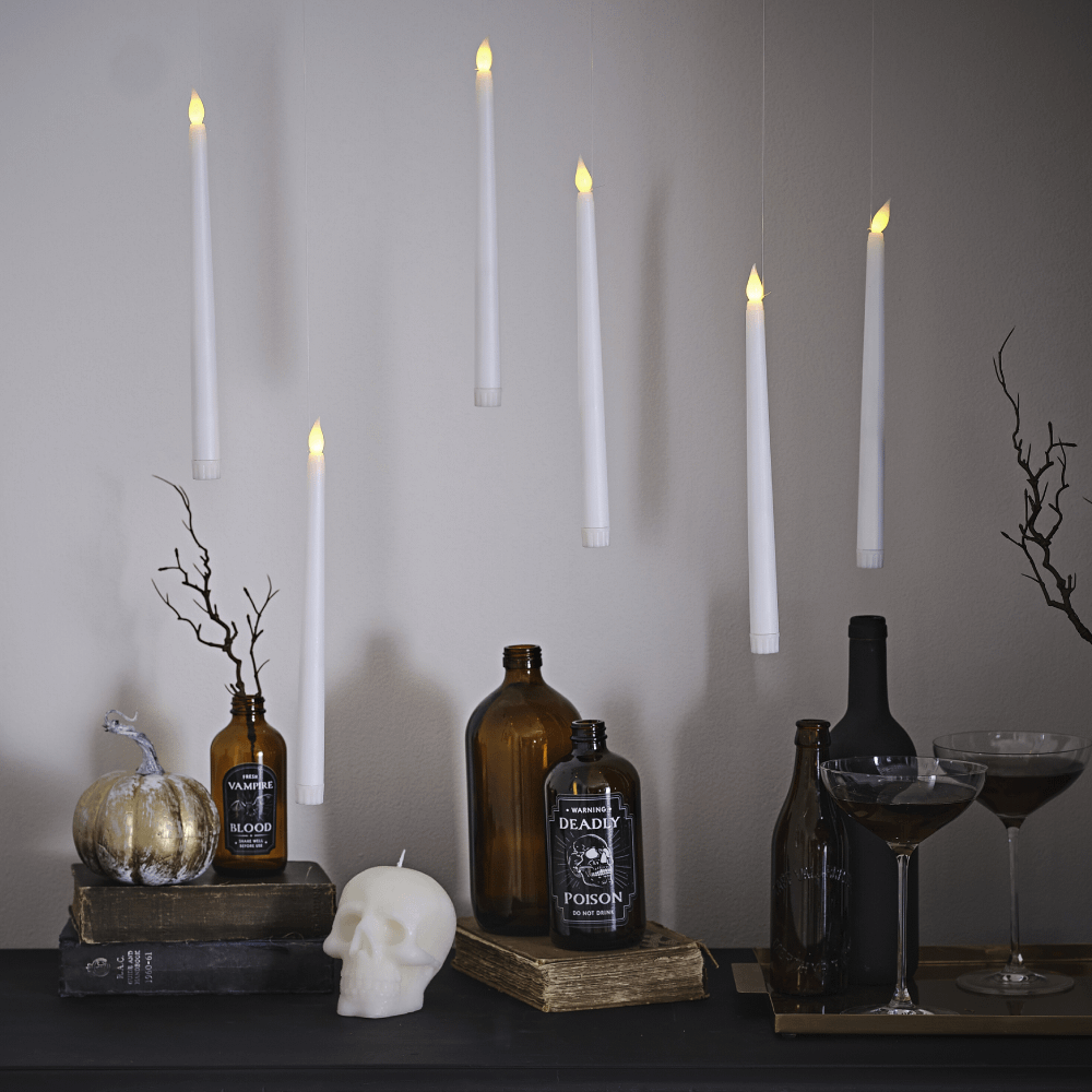 Zwevende, witte kaarsen met LED verlichting hangen boven een donkerbruine, houten tafel versierd met bruine glazen en een kaars in de vorm van een doodshoofd