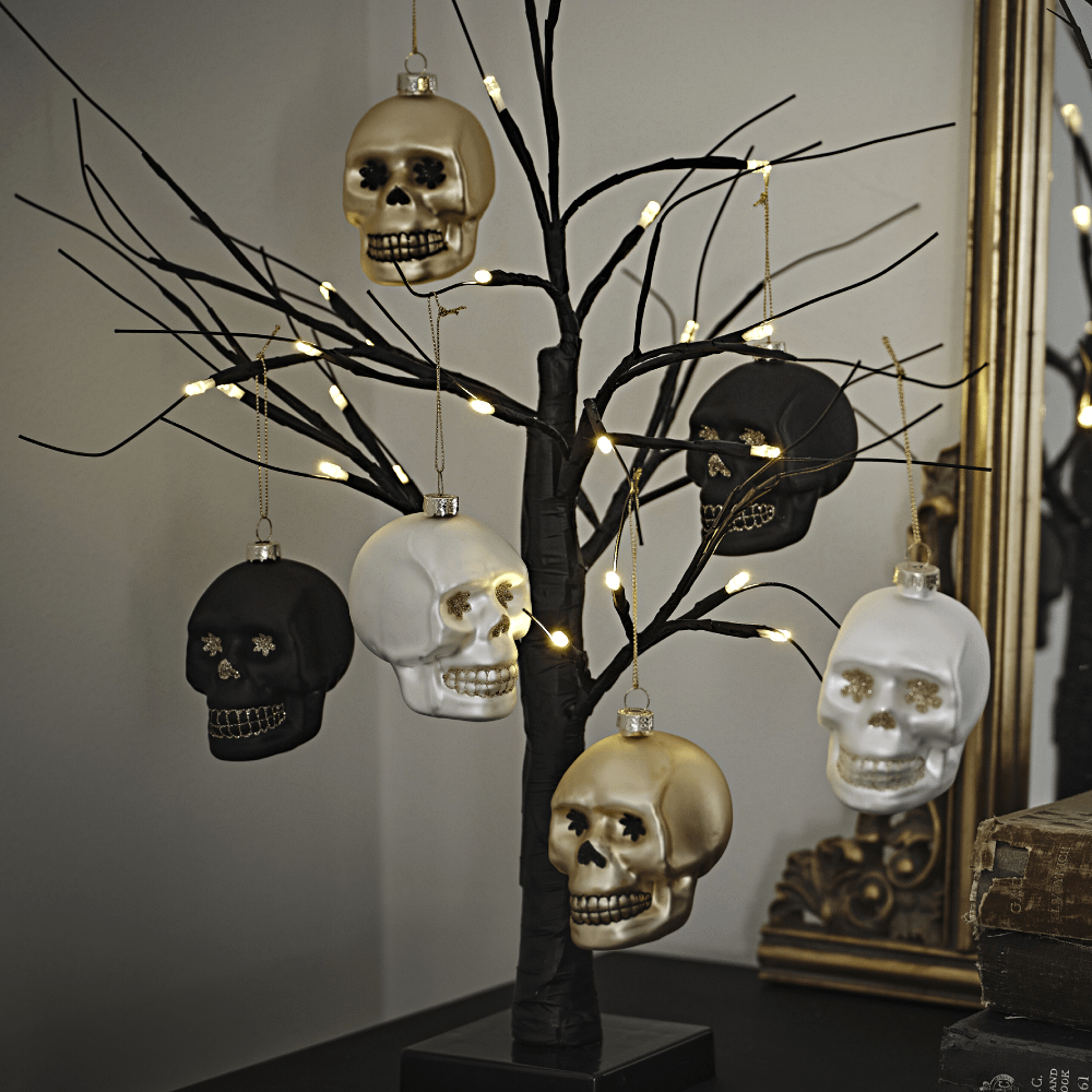 Kerstballen in de vorm van doodshoofden in het zwart, goud en wit mte glitters hangen in een zwarte, lichtgevende boom
