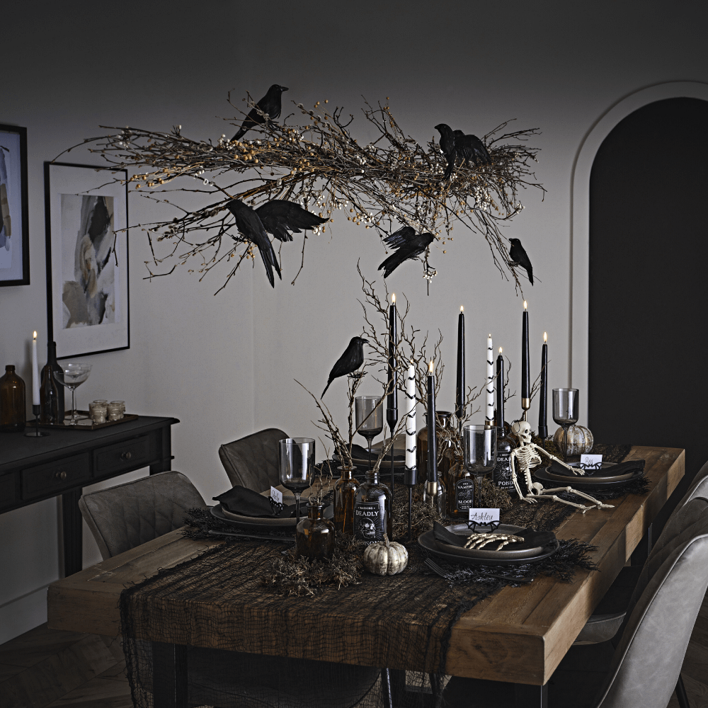Houten tafel versierd met kraaien en vleermuizen, zwarte en witte kaarsen en donkergroen mos