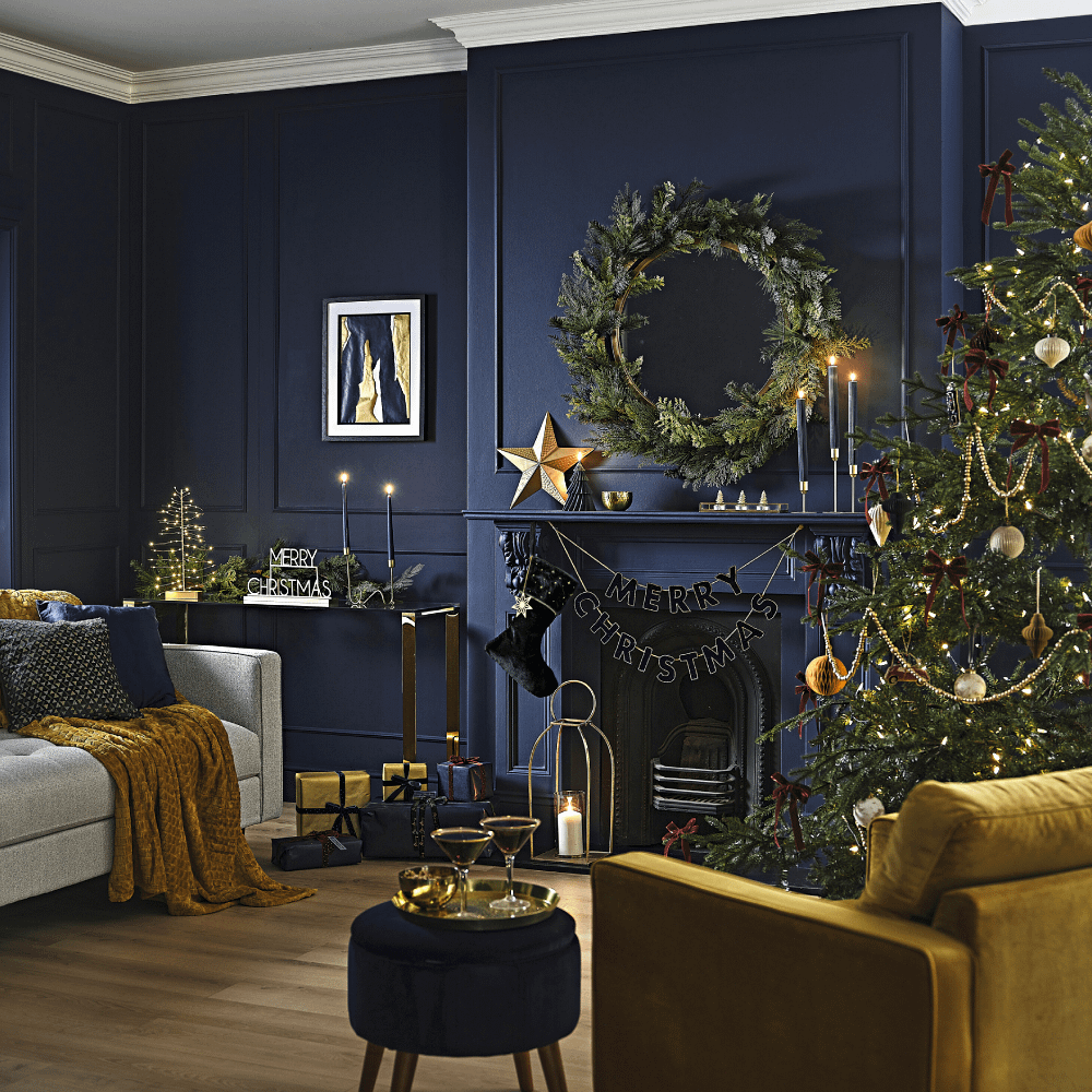 Woonkamer met openhaard en donkerblauwe muur is versierd met zwarte, donkergroene en gouden kerstversiering