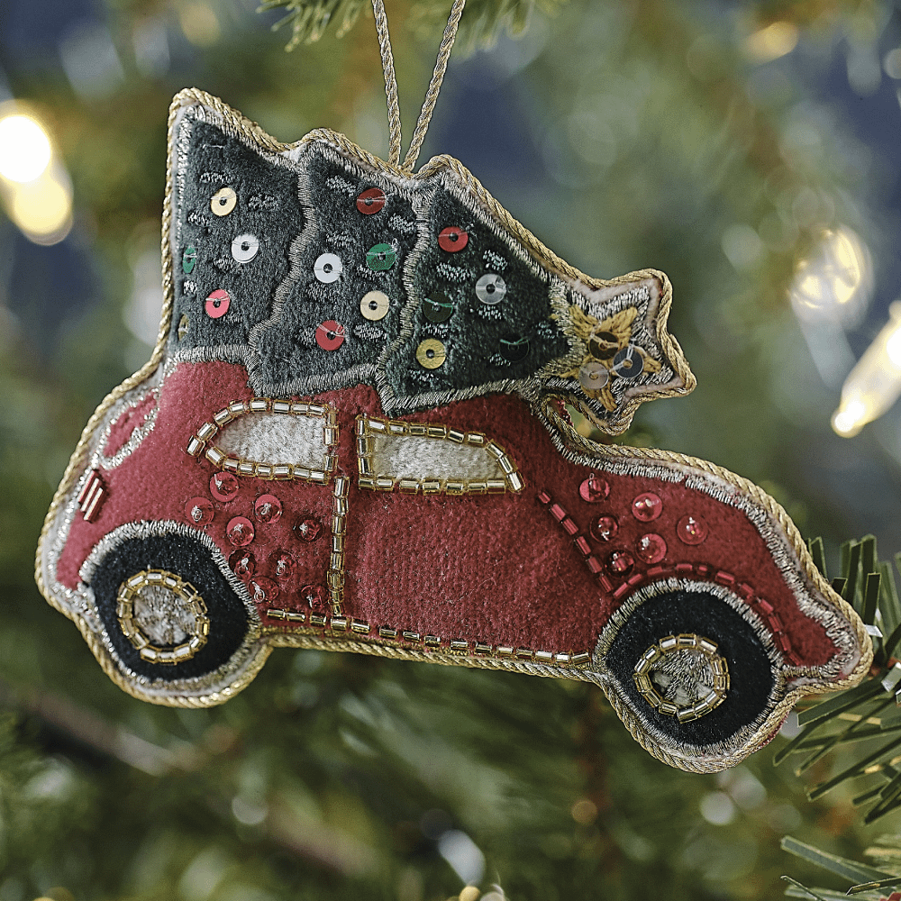 Kerstboomhanger in de vorm van een rode auto met een groen kerstboompje op het dak hangt in de boom