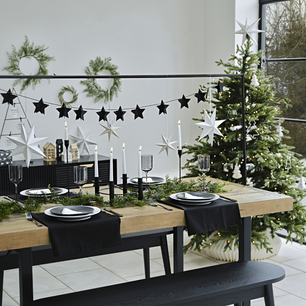 Een houten tafel versierd met zwarte kerst decoratie staat in een lichte ruimte bij een kerstboom