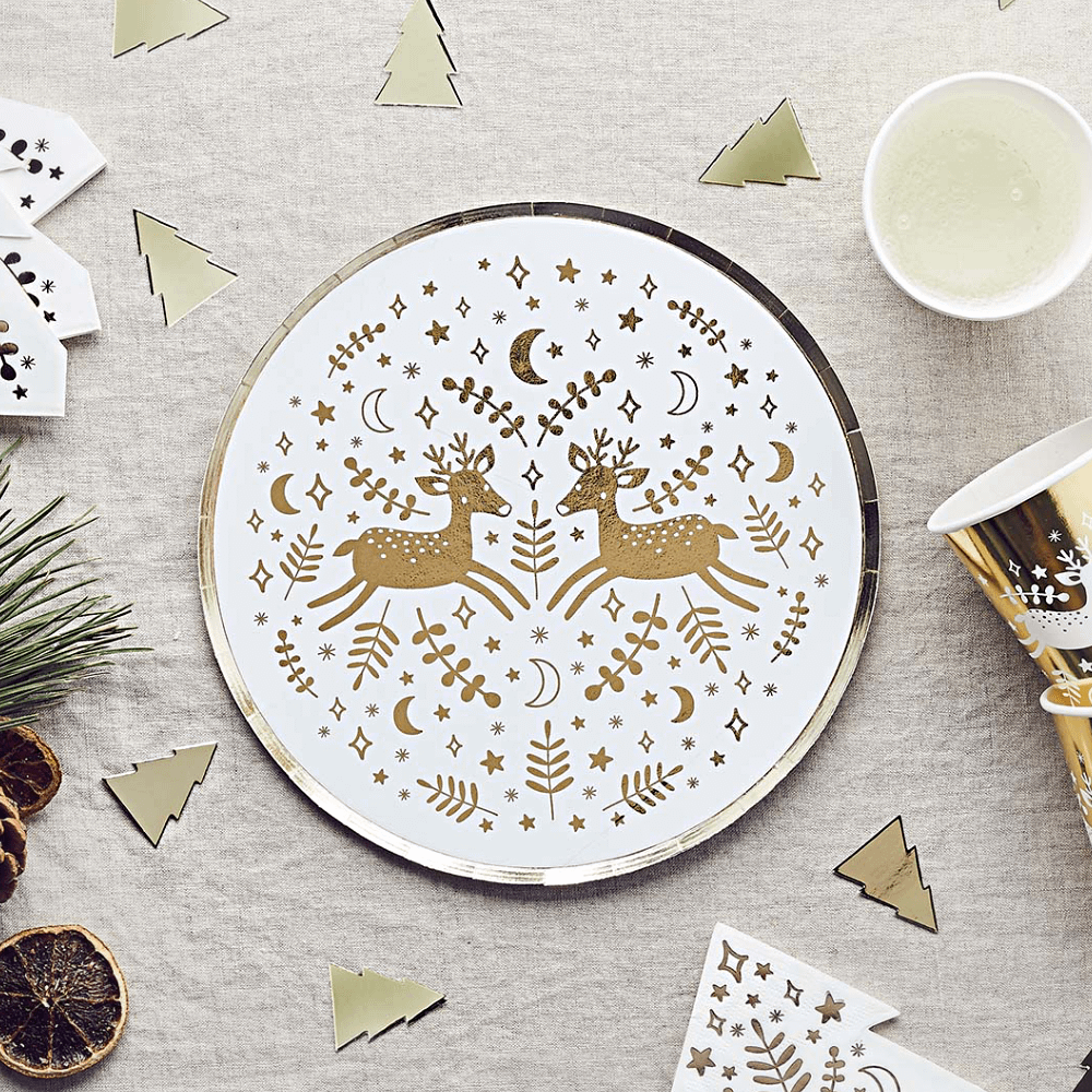 Wit bordje met gouden print en gouden rand ligt op een katoenen, beige tafellaken naast gouden confetti in de vorm van kerstbomen