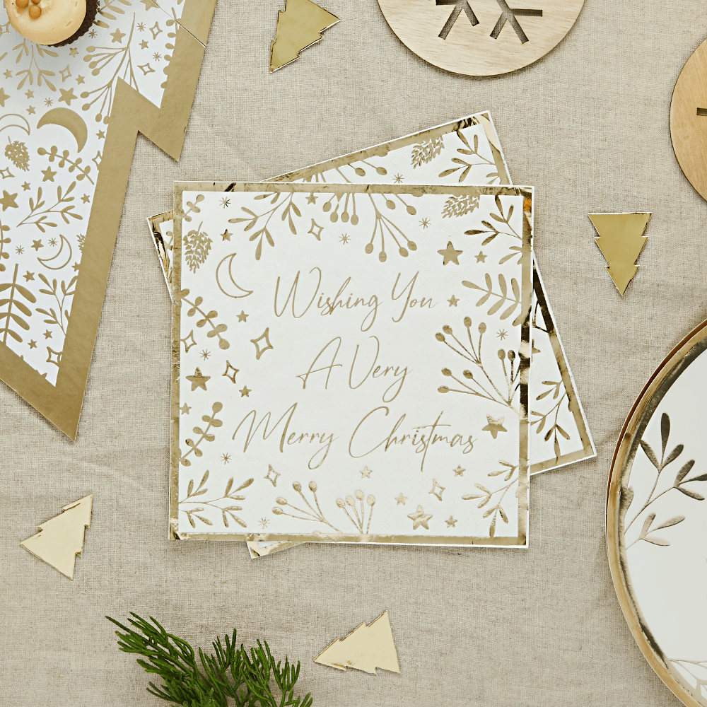 Servet in het wit en goud met de tekst wishing you a very merry christmas ligt op een jute tafelkleed met gouden confetti in de vorm van kerstbomen