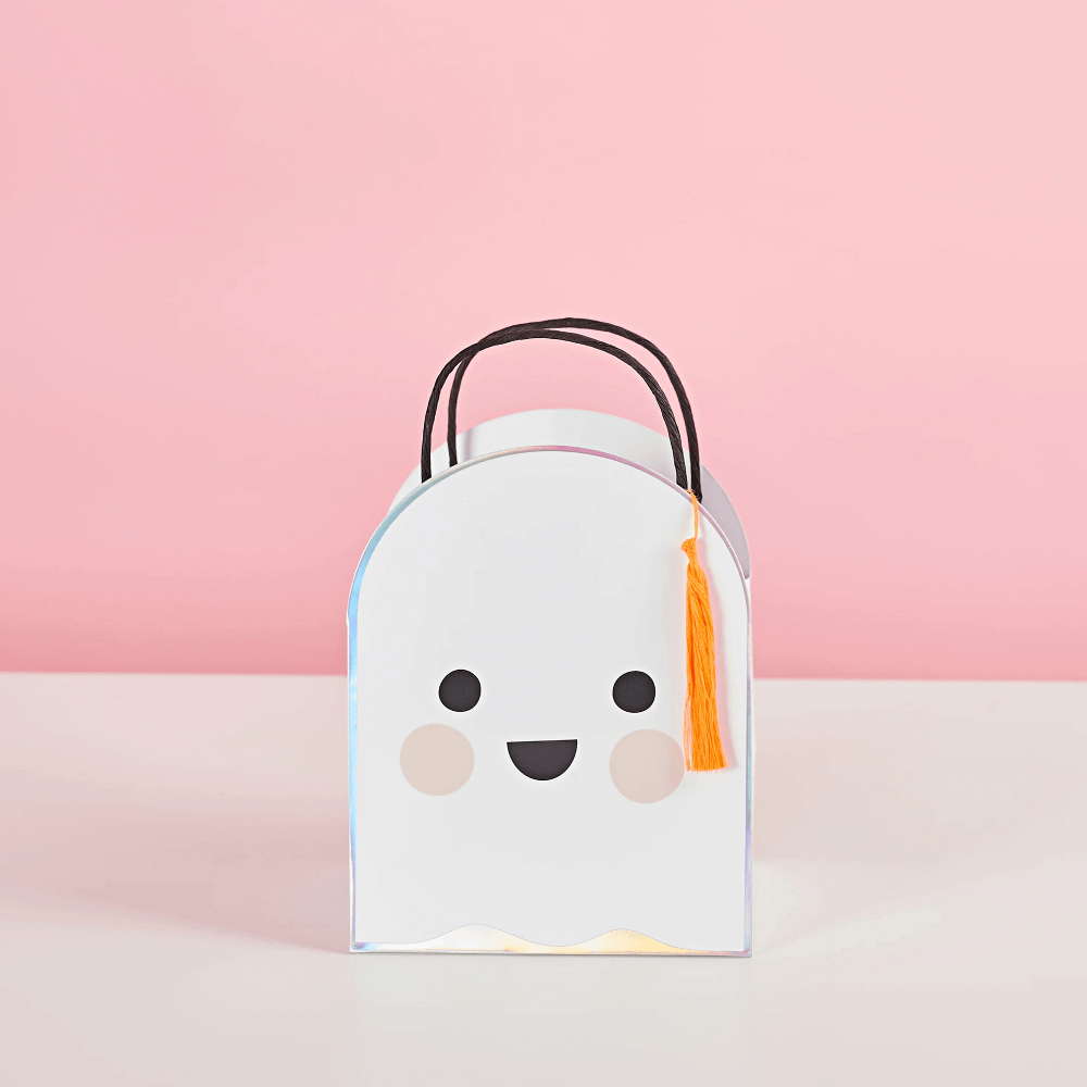 Cadeautas in de vorm van een spookje die lacht met een oranje tassel staat op een witte tafel voor een roze achtergrond