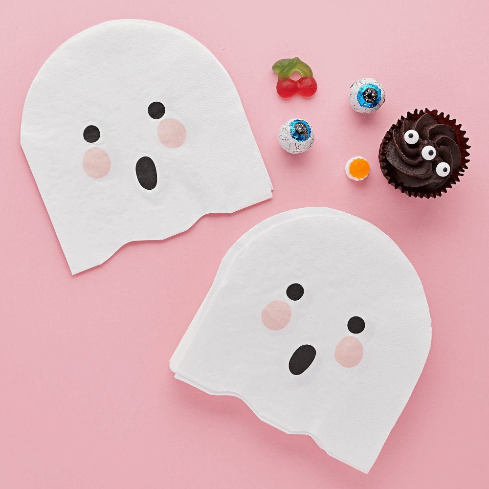 Servet in de vorm van een spook met een spookgezichtje liggen op een roze ondergrond naast een chocolade cupcake