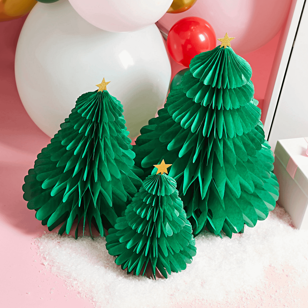Groene honeycombs in de vorm van kerstbomen met een gouden ster staan op nepsneeuw op een roze tafel