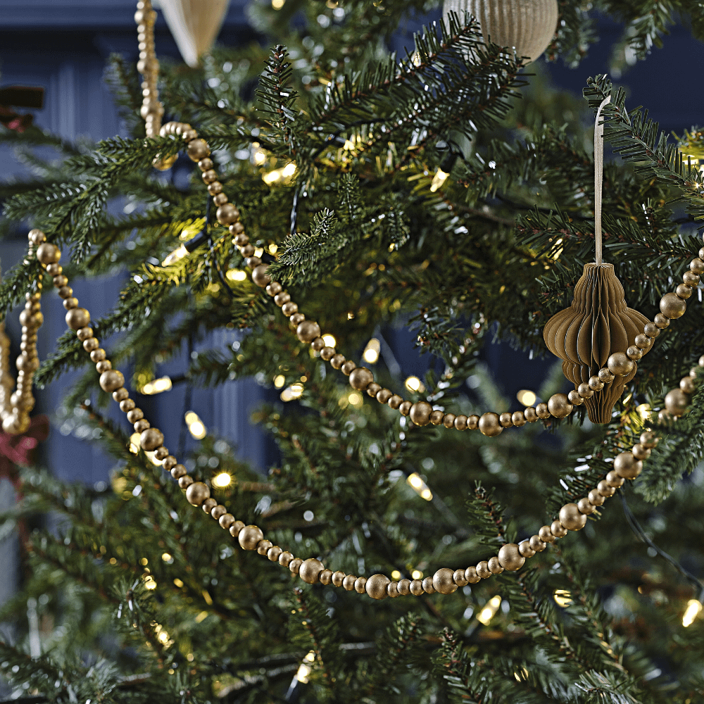 Gouden kralenslinger hangt in de kerstboom voor een marinablauwe muur