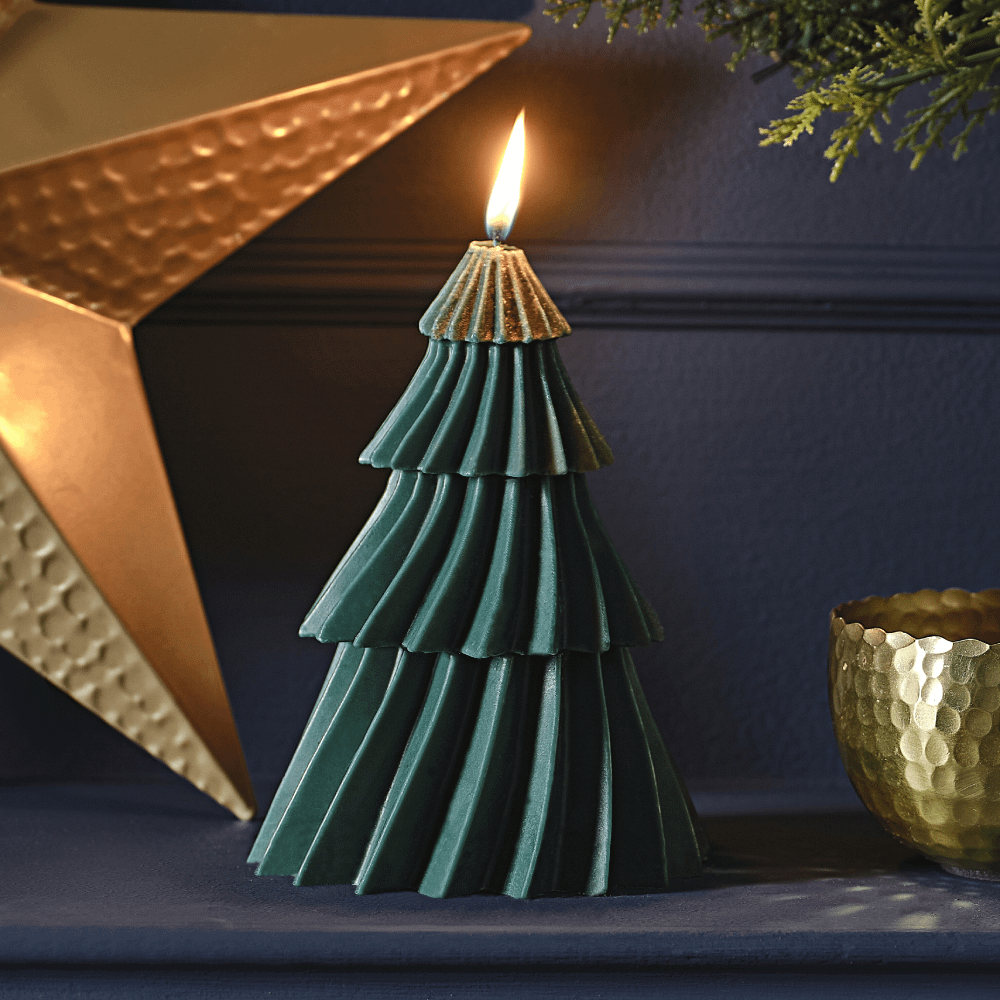 Donkergroene kaars in de vorm van een kerstboom staat op een marinablauwe haard voor een gouden, metalen ster