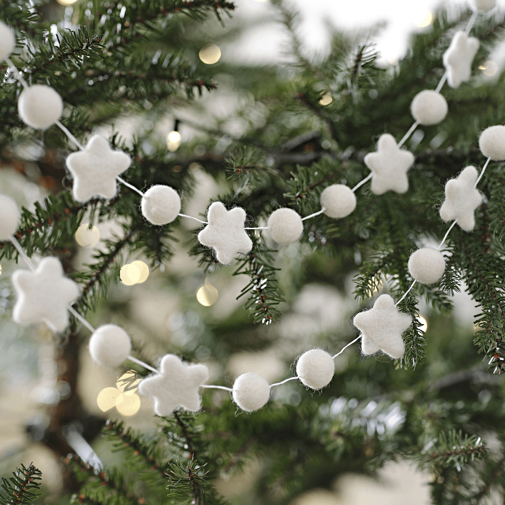 Witte slinger van stof met sterren en rondjes hangt in een groene kerstboom