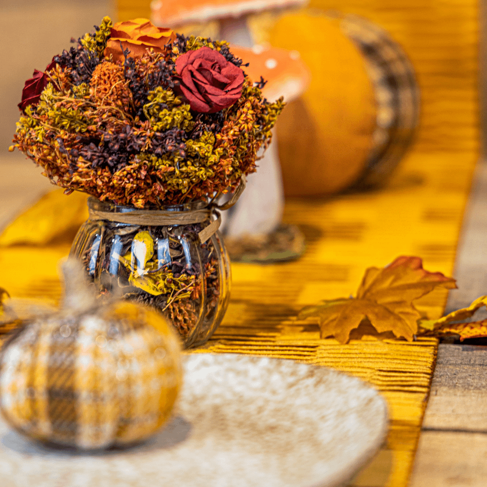 Gele tafelloper versierd met een stoffen pompoen, herfstbladeren en een rood, bruin en oranje herfstboeket