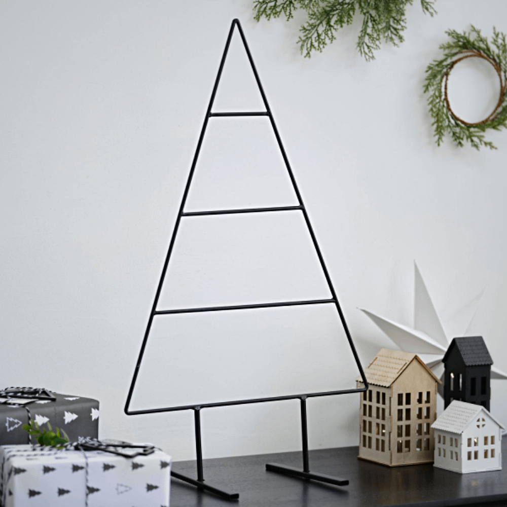 Metalen kerstboom in het zwart staat op een zwarte tafel naast houten huisjes