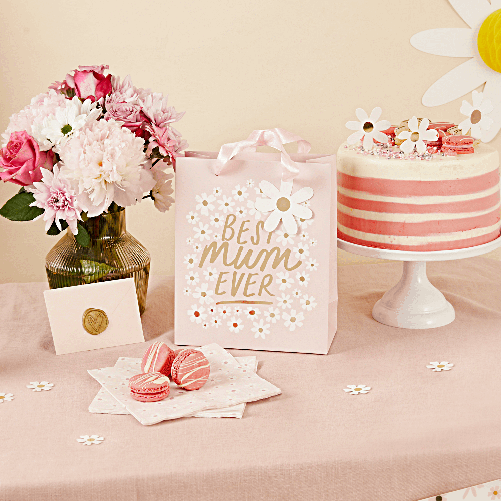 Roze cadeautasje met de gouden tekst best mum ever en madeliefjes staat voor een taart op een wit plateau